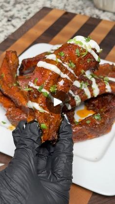 a person in black gloves holding up some food on a white plate with sauce and green garnishes