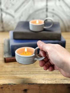 a person holding a small cup with a candle in it on a table next to books