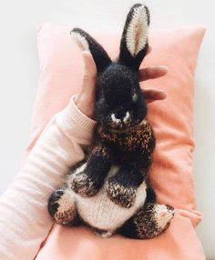 a stuffed animal sitting on top of a pink pillow next to a person's hand