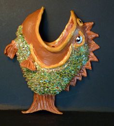 a ceramic figurine of a fish with green and orange leaves on it's head