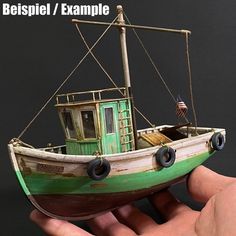 a hand holding a small model of a green and white boat