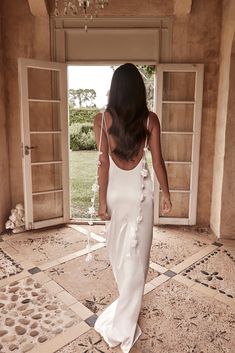 a woman in a white dress is walking through an open doorway with a chandelier hanging from the ceiling