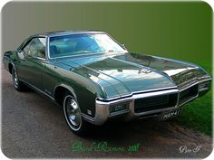 a green car parked on the side of a road next to a grass covered field