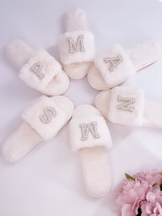 four pairs of white slippers with the letters n and m on them next to pink flowers