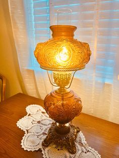 an antique lamp on a table in front of a window with crocheted doily