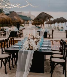 the table is set up on the beach for an ocean themed wedding reception with white flowers and blue napkins