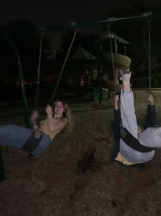 two people sitting on swings at night in the park, one holding onto another person's leg