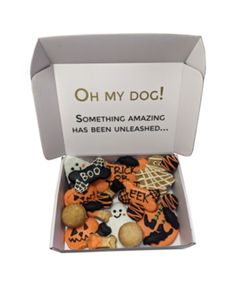 an open box filled with halloween cookies on top of a white table next to a sign that says oh my dog