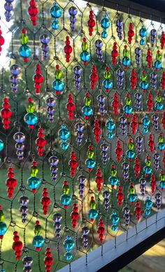 colorful glass beads hanging on the side of a window in front of a green yard