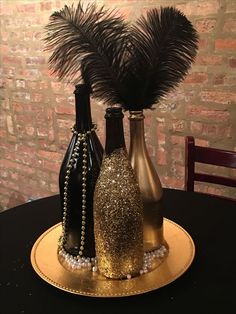 three bottles are sitting on a gold plate with feathers in them and beads around the bottle