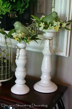 two white vases with flowers in them sitting on a table next to a birdcage