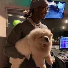 a man holding a white dog in front of a computer desk and sound mixing equipment