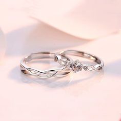 two wedding rings sitting on top of a white table next to a rose flower bouquet