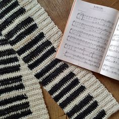 an open book is next to a crocheted scarf with music notes on it