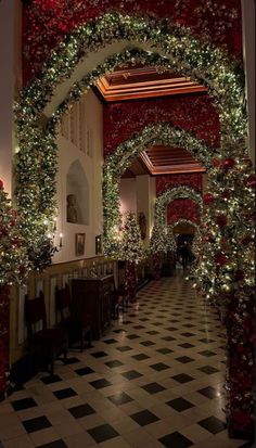 an archway decorated with christmas lights and greenery at the end of a hallway in a building