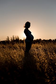 a pregnant woman standing in tall grass at sunset