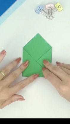 two hands are holding an origami piece on top of a table with scissors