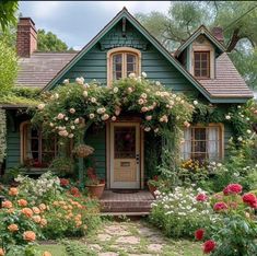 a green house with lots of flowers around the front door and steps leading up to it