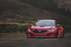 a red car parked on the side of a road next to some hills and trees