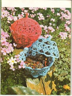 two crocheted baskets sitting on top of a wooden table in front of flowers