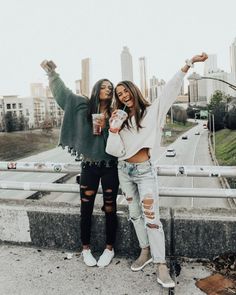 two women standing next to each other with their arms in the air and one holding a cup