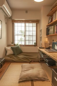 a bed sitting under a window next to a wooden shelf filled with books and other items