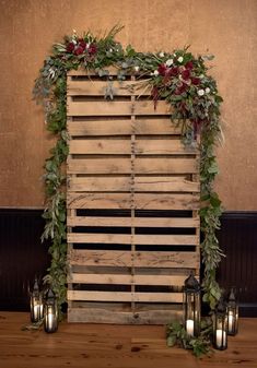 a wooden pallet with candles and greenery on it, sitting in front of a wall