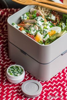 a lunch box with salad in it on a red and white tablecloth