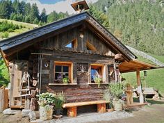 a small wooden cabin in the mountains with plants and potted plants on the porch