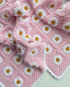 a crocheted blanket with white and yellow daisies on the edges is laying on a table