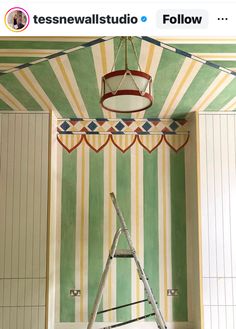 a ladder is in the corner of a room painted green and yellow with white stripes