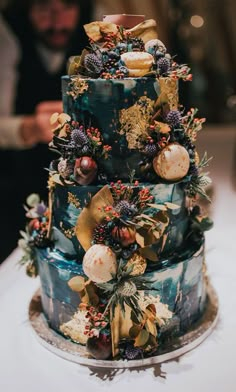 a multi - tiered cake decorated with fruits and leaves is on a white table