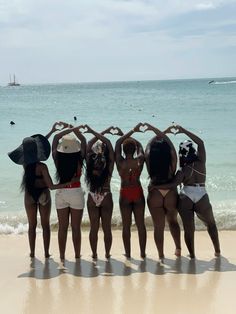 four women in bikinis stand on the beach with their hands up to heart shaped shapes