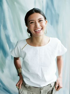 a woman standing in front of a blue backdrop smiling at the camera with her hands on her hips