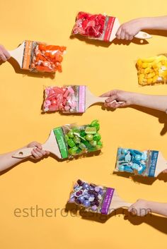 four people holding small bags of candy on top of a yellow surface with one person's hand reaching for them