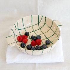 berries and blueberries sit in a bowl on a white tablecloth with green lines