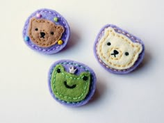 three little felt buttons with faces on them, one has a bear and the other is a frog