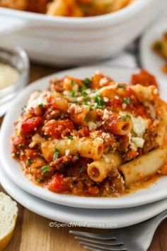 pasta with meat and sauce on a white plate next to garlic bread, parmesan