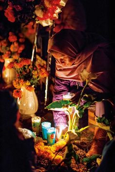 a woman kneeling down next to flowers and candles