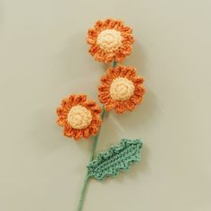 three crocheted flowers on a white surface with one flower attached to the end