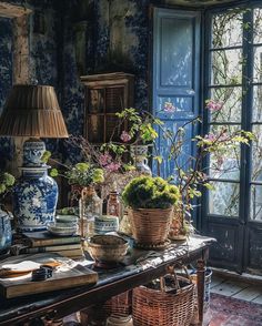 a table with vases and plants on it in front of a blue wallpapered room