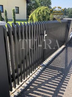 a black metal fence in front of a house with trees and bushes on the side