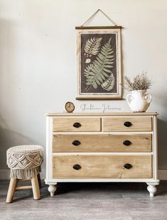 a white dresser with drawers and a plant on top of it next to a stool