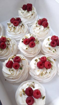 there are many cupcakes with white frosting and raspberries on top