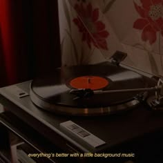 a record player sitting on top of a table next to a red flowered wall