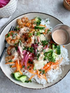 a white plate topped with rice, shrimp and veggies next to a bowl of sauce