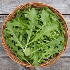 a basket filled with green leafy greens on top of a wooden table