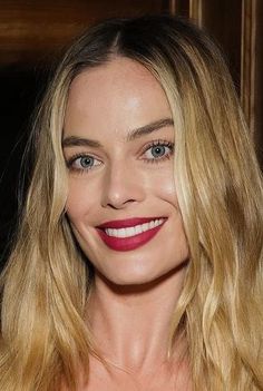 a woman with long blonde hair and blue eyes smiles at the camera while wearing a red dress