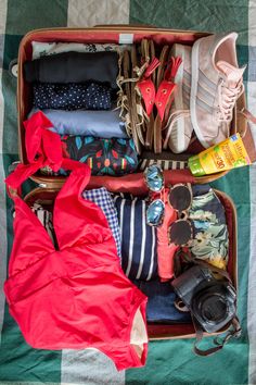 an open suitcase filled with clothing and shoes on top of a checkered table cloth