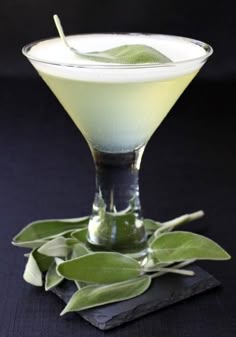 a glass filled with a green liquid and topped with leaves on a black table cloth